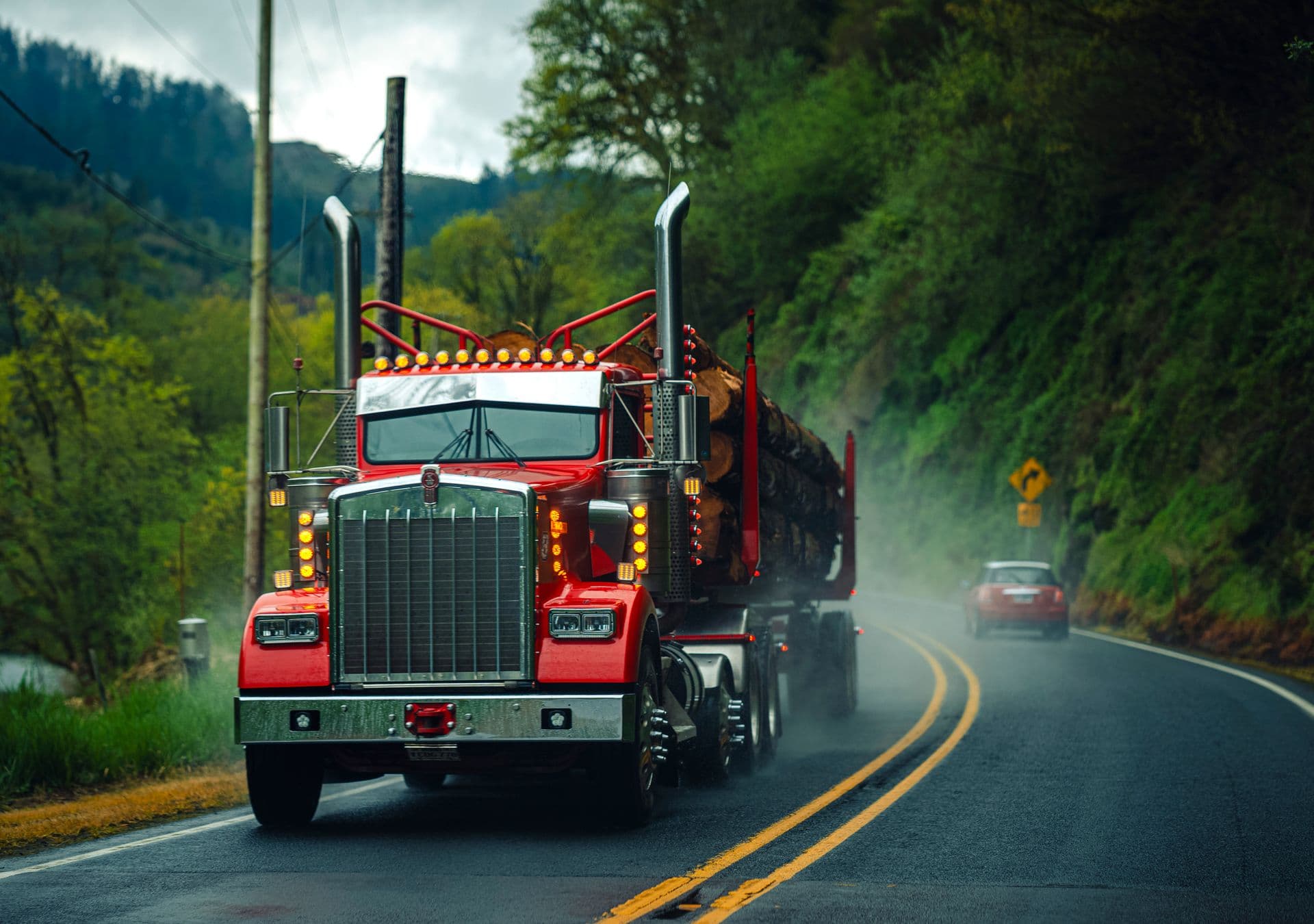 Red Kenworth log truck running a misty forest highway