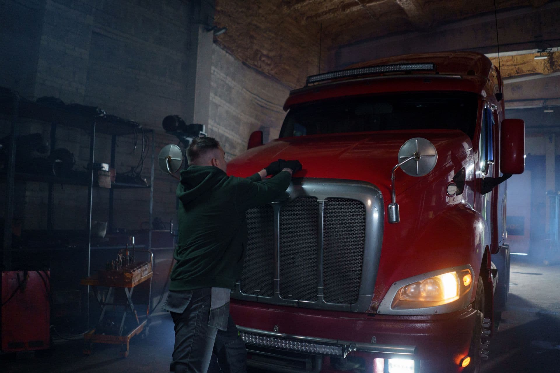 Mechanic working on a red semi truck in a dark garage