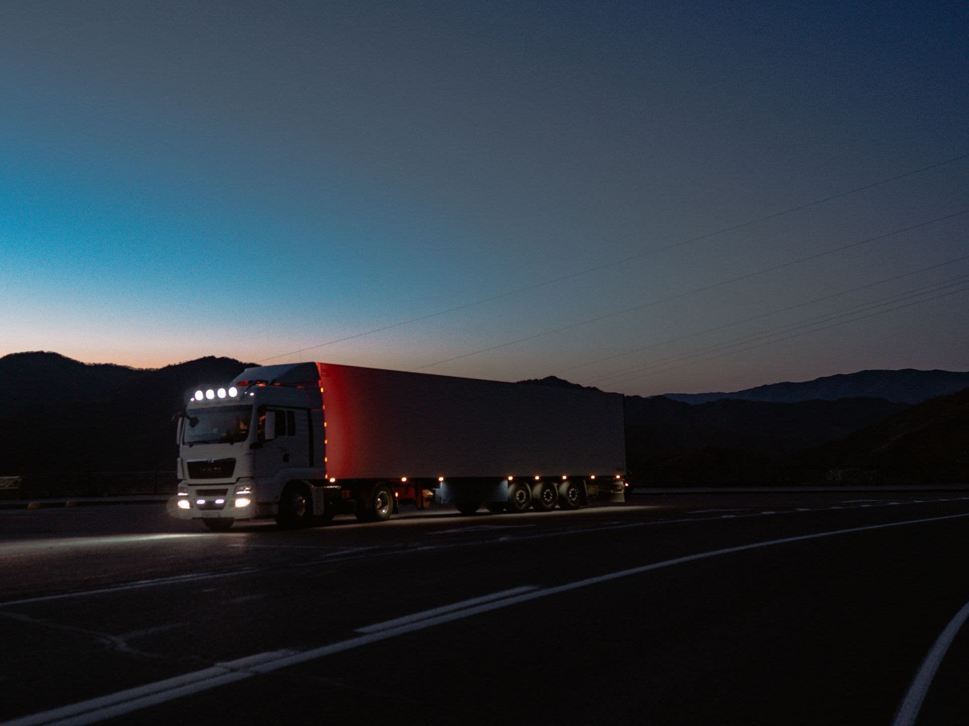 Semi truck with glowing red trailer lights on a dark highway at dusk