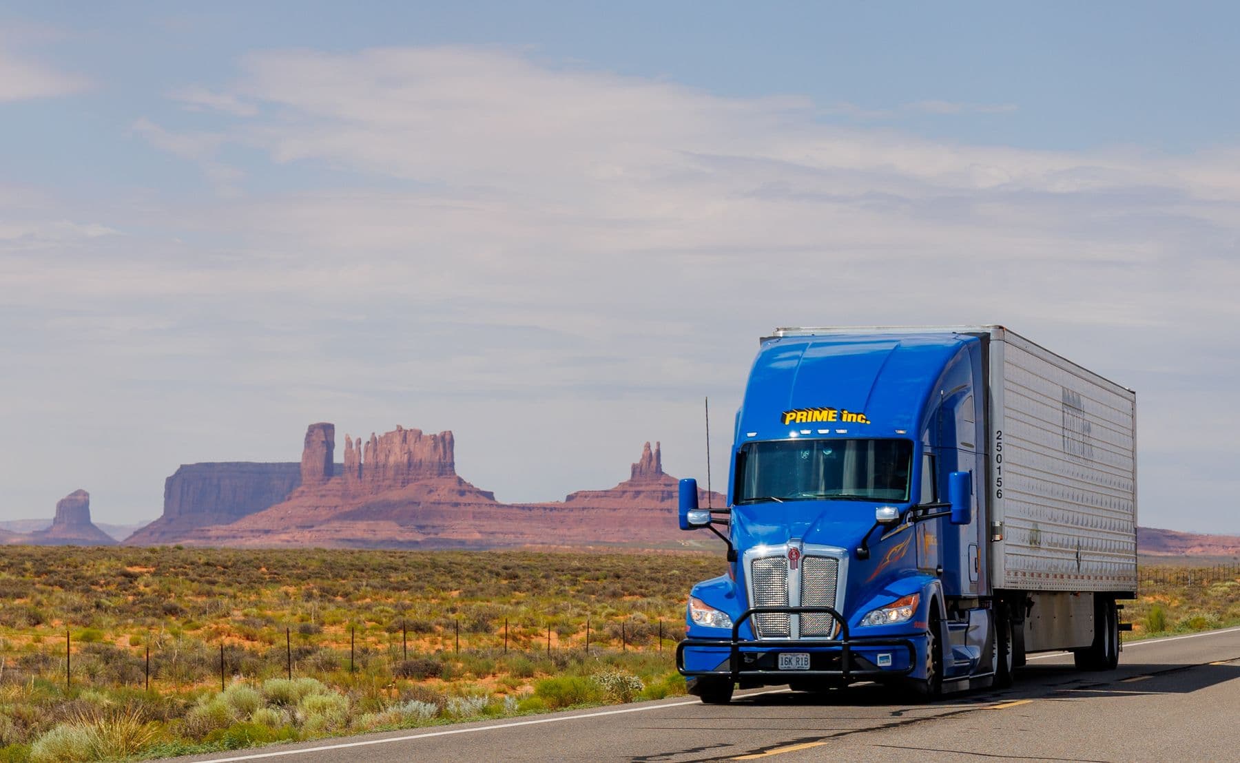 Truck running a desert highway past red rock mesas